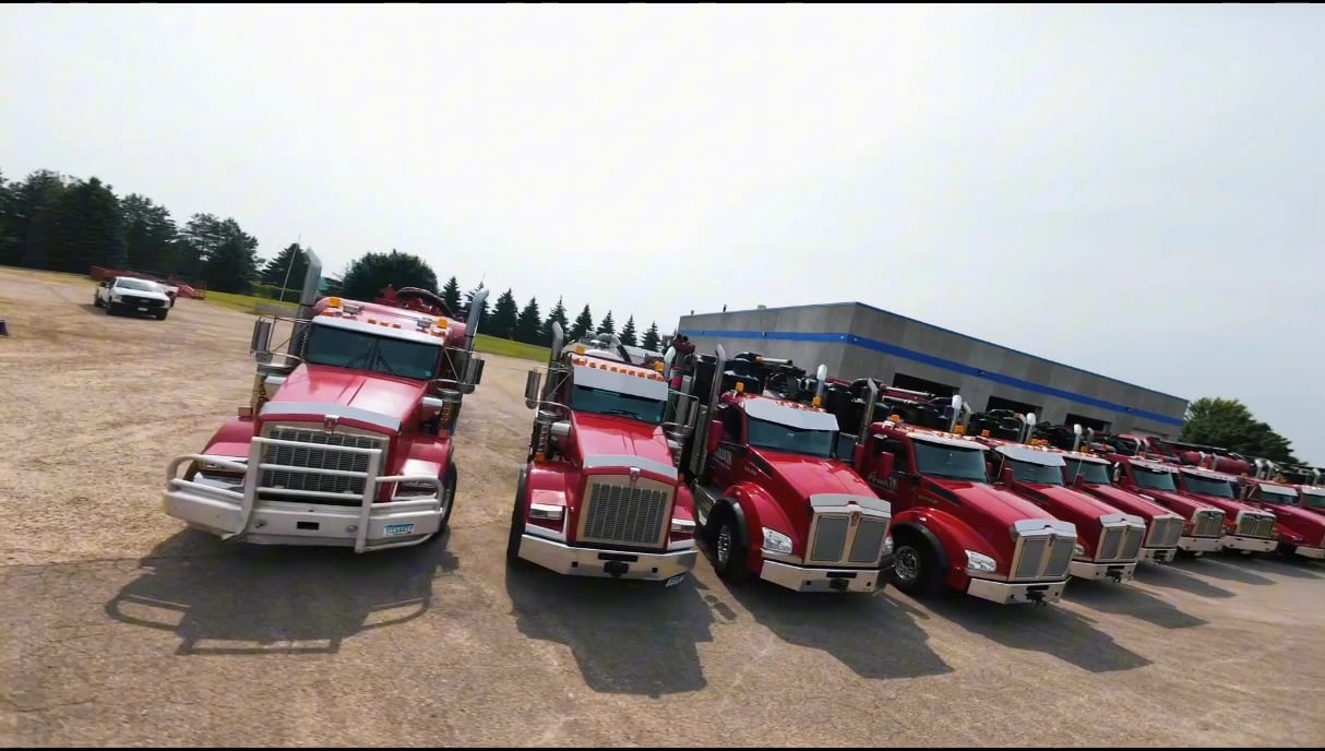 The fronts of three red Goliath Hydrovac trucks with the rest of the fleet and shop behind them