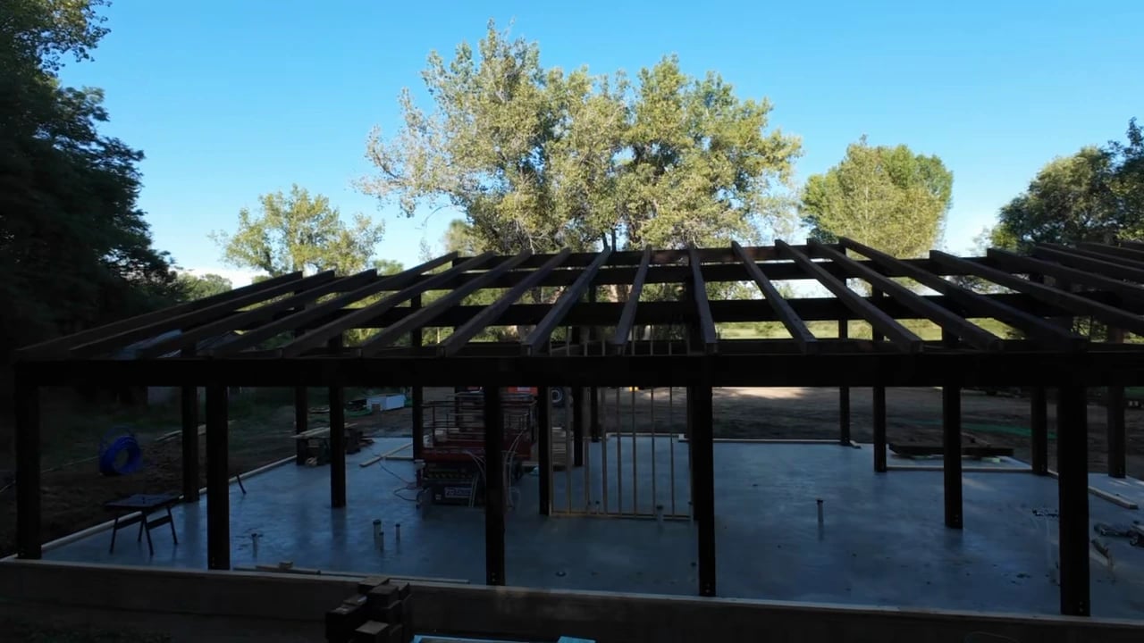 The assembled timber roof structure with trees and blue sky beyond